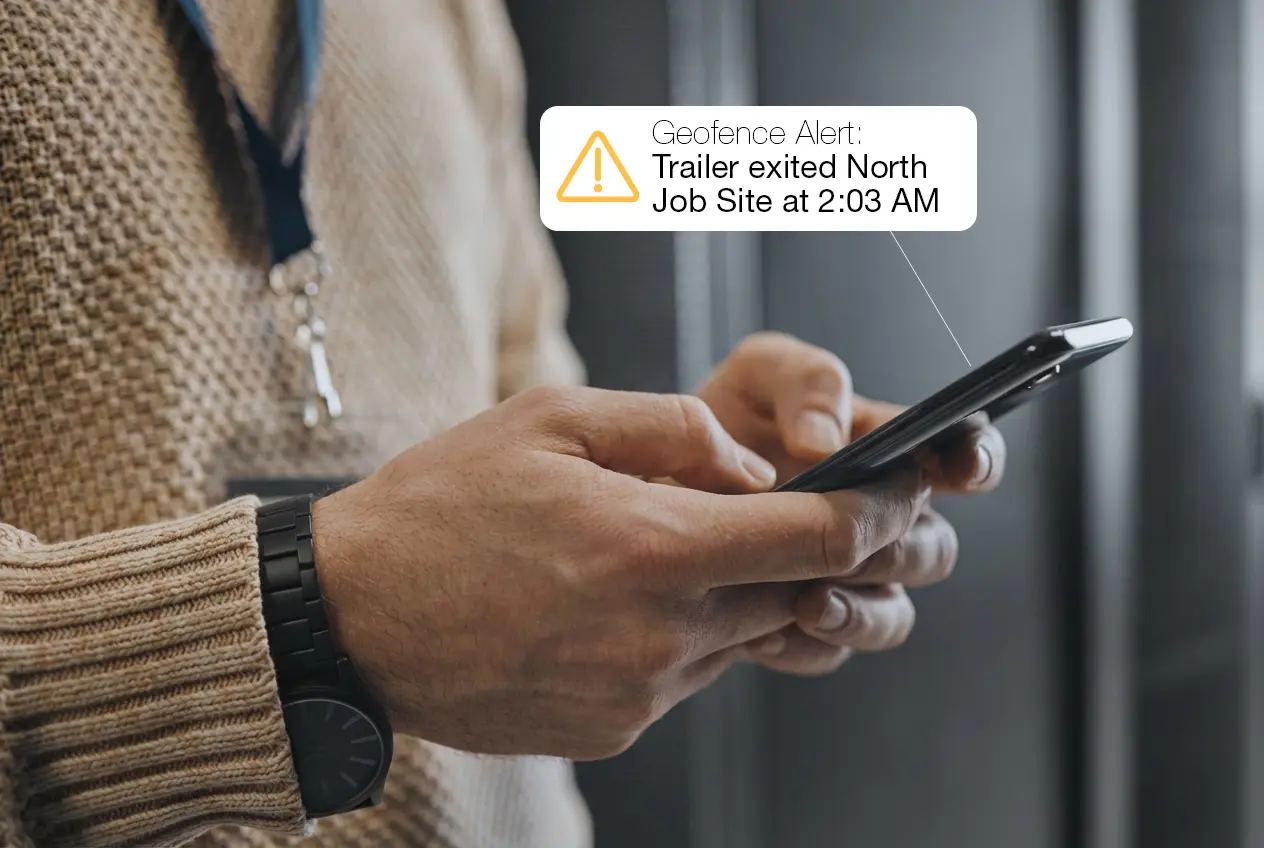 Person holding a smartphone receiving a geofence alert notification about a trailer exiting a jobsite after hours